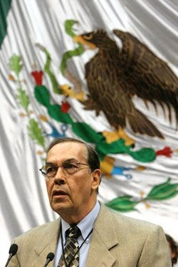 Dr. Roberto Rosas speaking at a podium before a Mexican flag